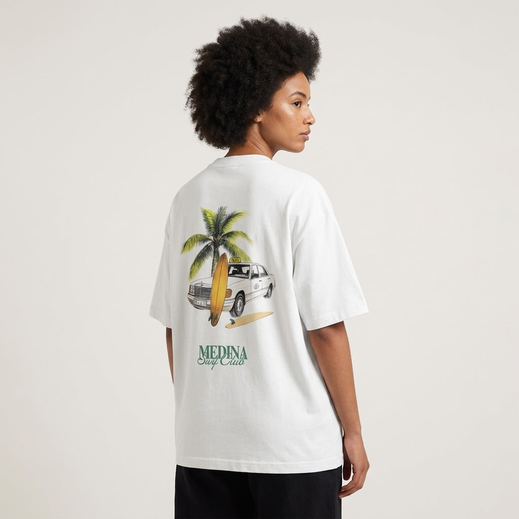 woman wearing a white t-shirt with a palm tree and car graphic on the back, standing against a plain background.
