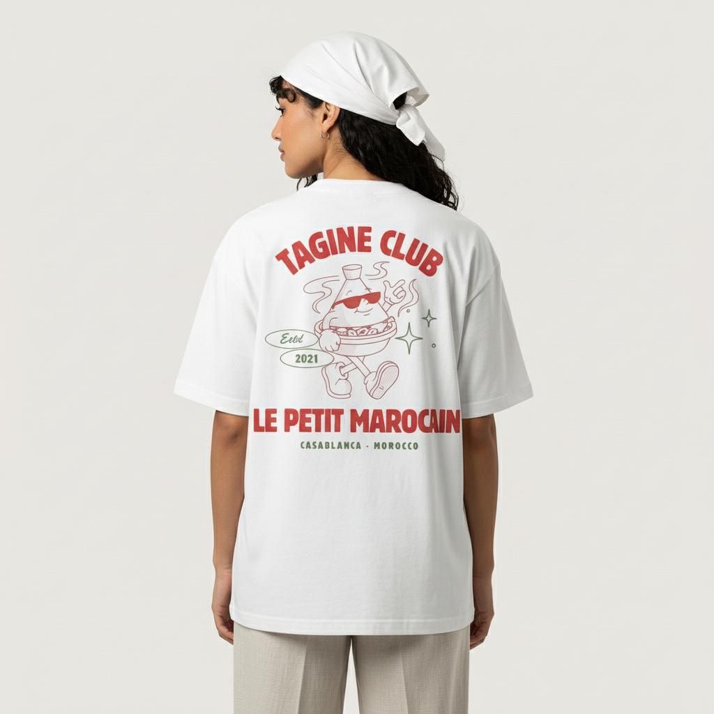 Moroccan woman wearing a white  heavyweight t-shirt featuring a retro cartoon mascot of a walking tagine with sunglasses, 'TAGINE CLUB' red text, and 'LE PETIT MAROCAIN' branding, vintage streetwear fit and standing against a plain background.