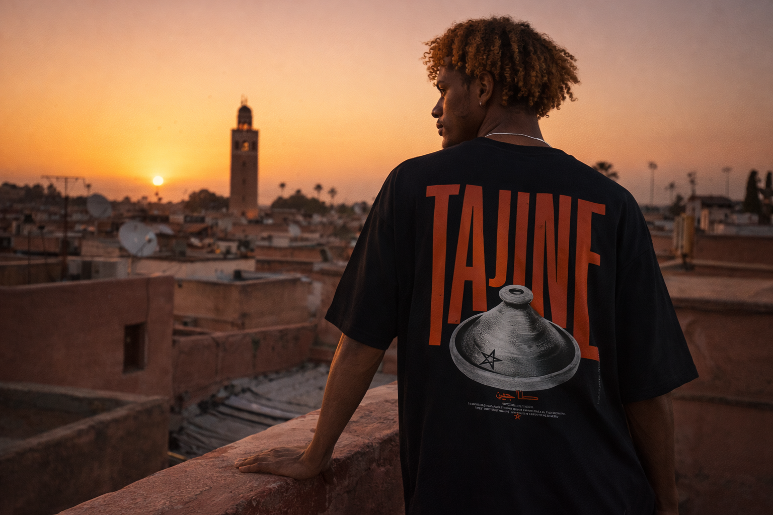 Person wearing a black t-shirt with 'Taine' branding overlooking a sunset over a cityscape.