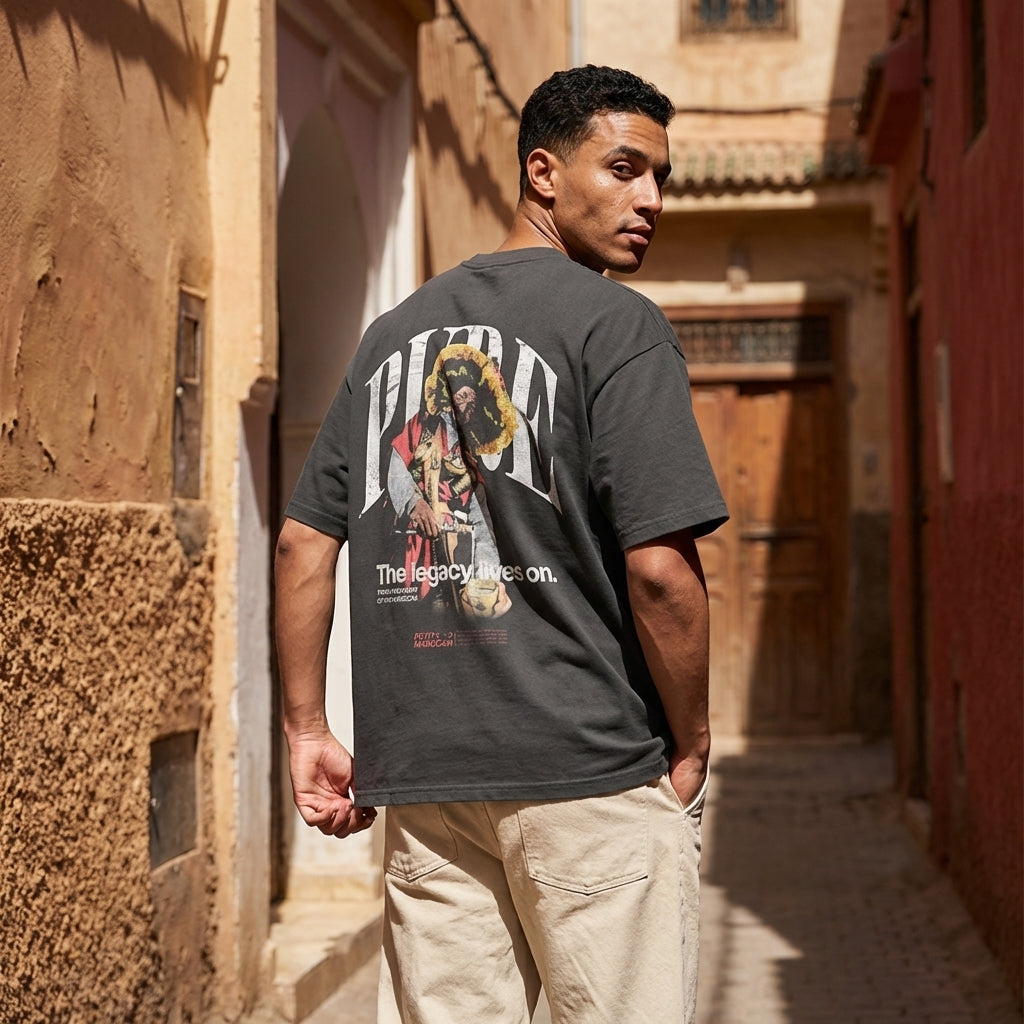 Man wearing Guerrab traditional water seller graphic on premium black t-shirt, standing in an alleyway architectural setting.