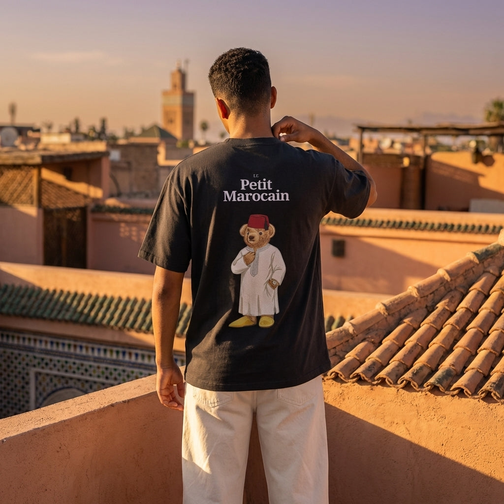 Person wearing a t-shirt with a bear graphic and 'Petit Marocain' text on a rooftop with cityscape in the background.